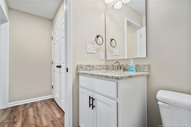 half bath with toilet, baseboards, wood finished floors, and vanity