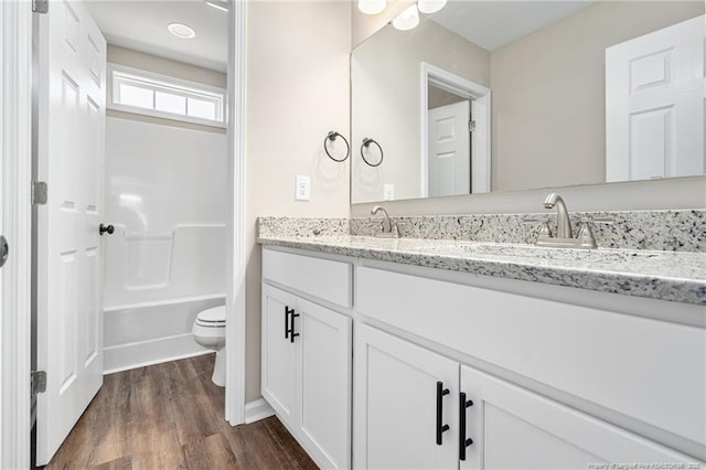 bathroom with toilet, a sink, double vanity, and wood finished floors