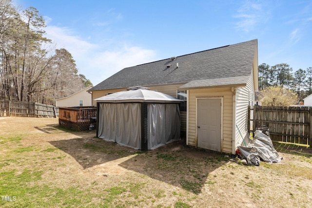 exterior space featuring roof with shingles, a fenced backyard, a gazebo, a storage unit, and a deck