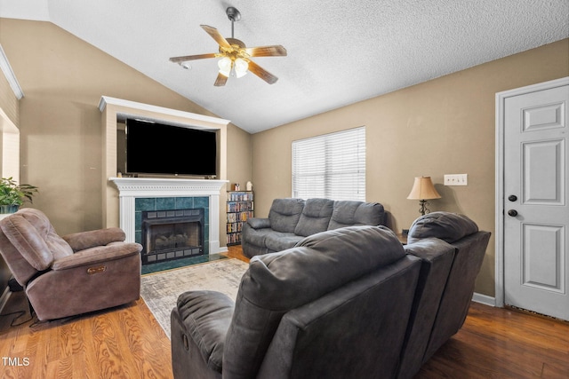 living area with a ceiling fan, a tile fireplace, a textured ceiling, wood finished floors, and vaulted ceiling