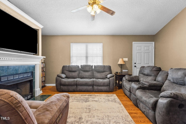 living room featuring a tiled fireplace, a textured ceiling, a ceiling fan, and wood finished floors