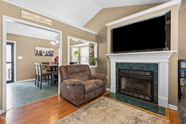 living area with a notable chandelier, wood finished floors, baseboards, vaulted ceiling, and a tile fireplace