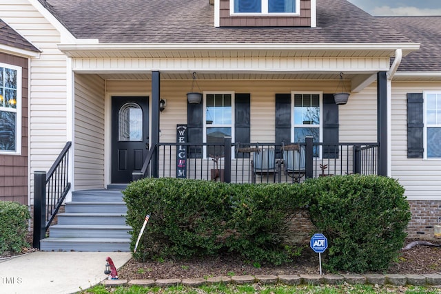 view of exterior entry with a porch and roof with shingles