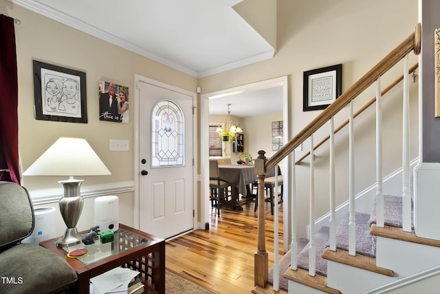 entryway featuring stairs, an inviting chandelier, light wood-type flooring, and ornamental molding