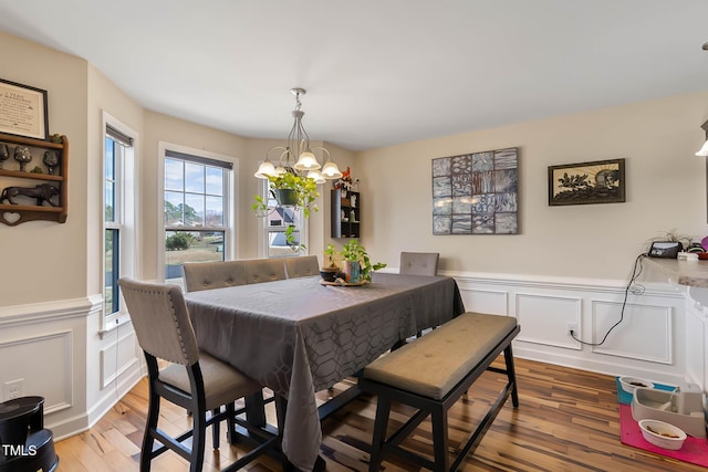 dining area with a notable chandelier, wood finished floors, and wainscoting