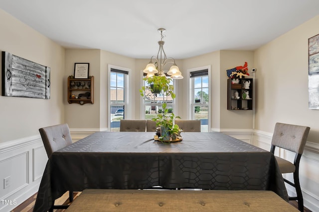 dining room with a wealth of natural light, a notable chandelier, wainscoting, and a decorative wall