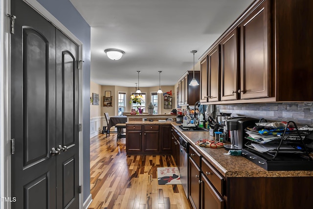 kitchen with a peninsula, dark brown cabinets, light wood-style floors, dishwasher, and dark countertops