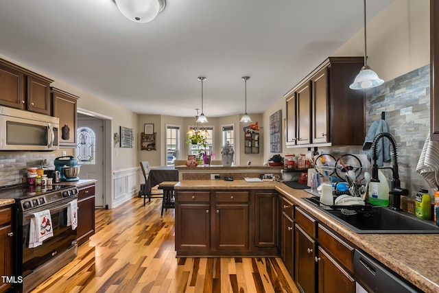 kitchen with light wood-type flooring, a wainscoted wall, a sink, stainless steel appliances, and a peninsula