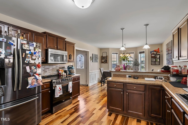 kitchen featuring a wainscoted wall, decorative light fixtures, stainless steel appliances, light wood-style floors, and dark brown cabinetry