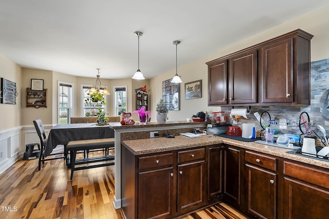 kitchen with dark brown cabinets, a wainscoted wall, light wood-type flooring, a peninsula, and hanging light fixtures