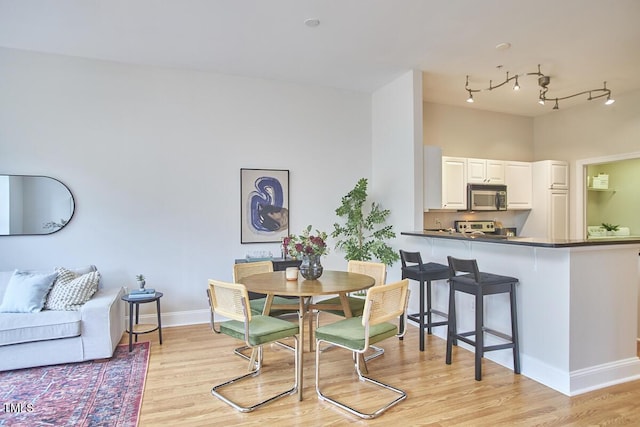 dining area with light wood-type flooring, baseboards, and track lighting