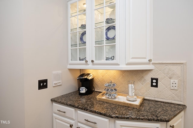 interior space with glass insert cabinets, white cabinets, backsplash, and dark stone counters