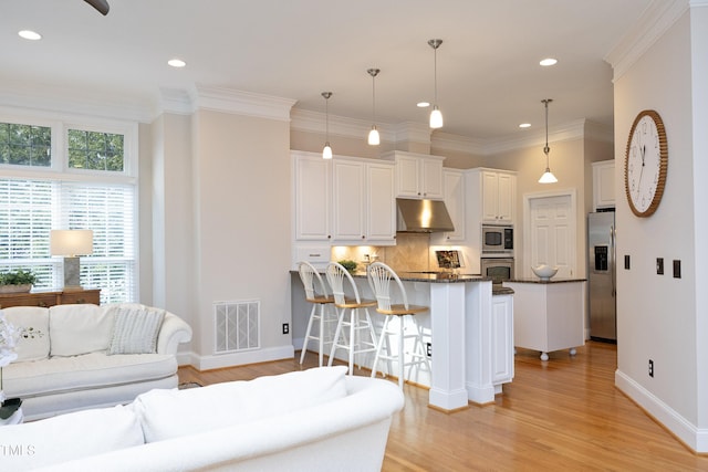 kitchen with under cabinet range hood, stainless steel appliances, a peninsula, visible vents, and a healthy amount of sunlight