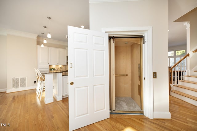 interior space with visible vents, a kitchen breakfast bar, white cabinetry, ornamental molding, and light wood finished floors