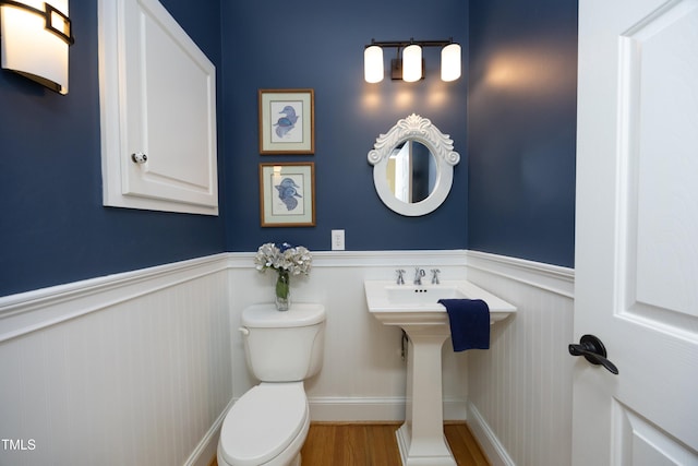 half bathroom featuring a wainscoted wall, wood finished floors, and toilet