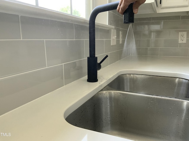 interior details featuring a sink, light countertops, decorative backsplash, and white cabinets