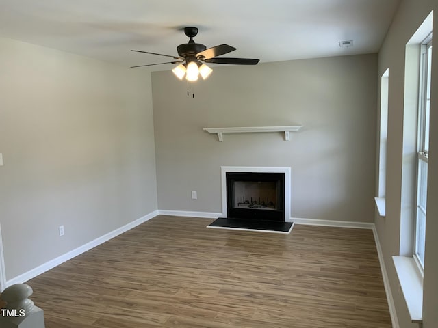 unfurnished living room with baseboards, a fireplace with raised hearth, a ceiling fan, and wood finished floors