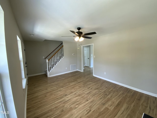 unfurnished living room featuring visible vents, wood finished floors, baseboards, ceiling fan, and stairway