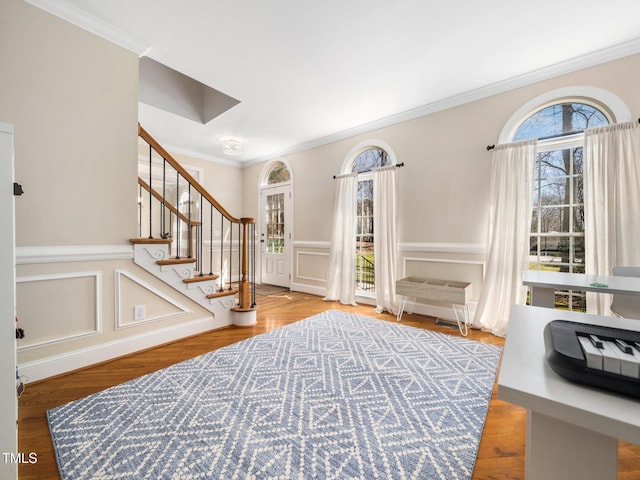 entryway with stairway, wood finished floors, a decorative wall, and ornamental molding