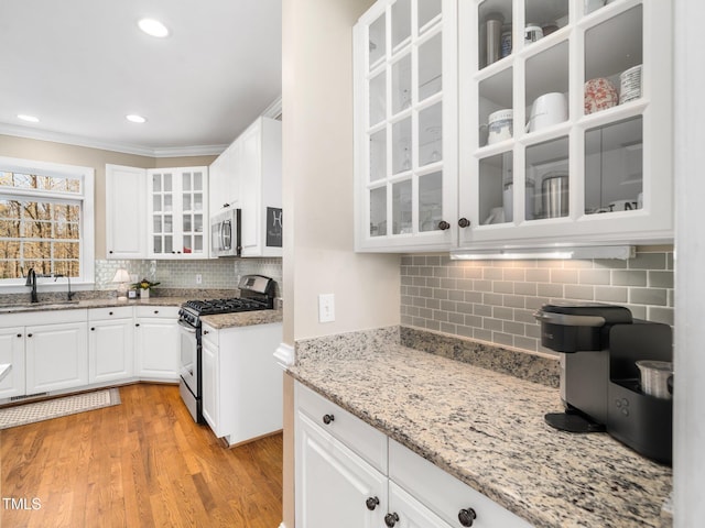 kitchen featuring light wood-type flooring, a sink, appliances with stainless steel finishes, white cabinets, and light stone countertops