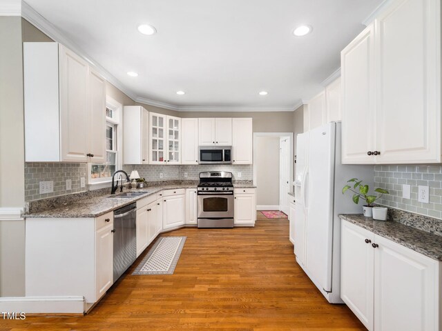 kitchen with a sink, ornamental molding, stainless steel appliances, white cabinets, and light wood-style floors