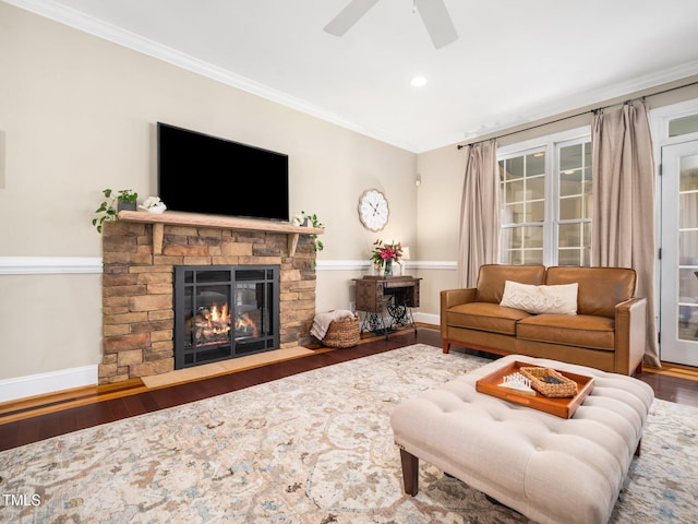 living area with a stone fireplace, ornamental molding, baseboards, and wood finished floors