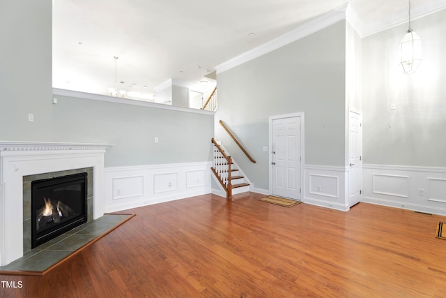 unfurnished living room featuring wood finished floors, a lit fireplace, stairs, crown molding, and a notable chandelier