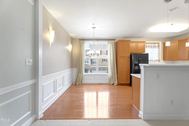 kitchen featuring light wood-style flooring, black refrigerator with ice dispenser, light countertops, a chandelier, and pendant lighting