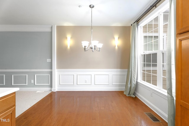 unfurnished dining area featuring a wainscoted wall, visible vents, a notable chandelier, and wood finished floors