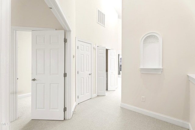 hall featuring a high ceiling, carpet flooring, visible vents, and baseboards