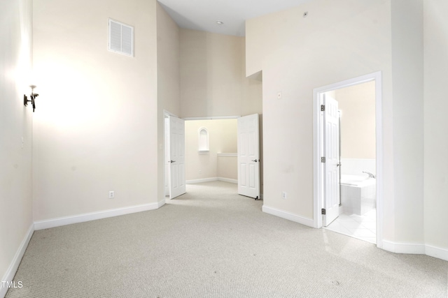 unfurnished bedroom featuring carpet floors, baseboards, a towering ceiling, and visible vents