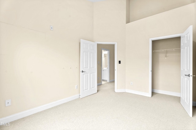 unfurnished bedroom featuring a high ceiling, a closet, light colored carpet, and baseboards