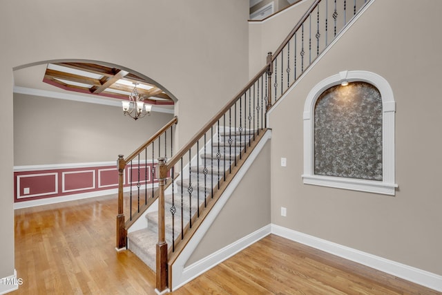 staircase featuring arched walkways, coffered ceiling, wood finished floors, and a chandelier