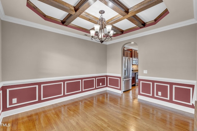 spare room featuring light wood-style floors, arched walkways, coffered ceiling, and an inviting chandelier