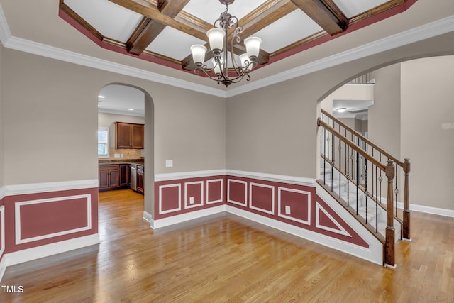 empty room featuring arched walkways, light wood finished floors, an inviting chandelier, coffered ceiling, and stairs