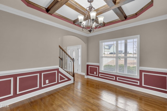 foyer entrance featuring arched walkways, a wainscoted wall, an inviting chandelier, wood finished floors, and coffered ceiling