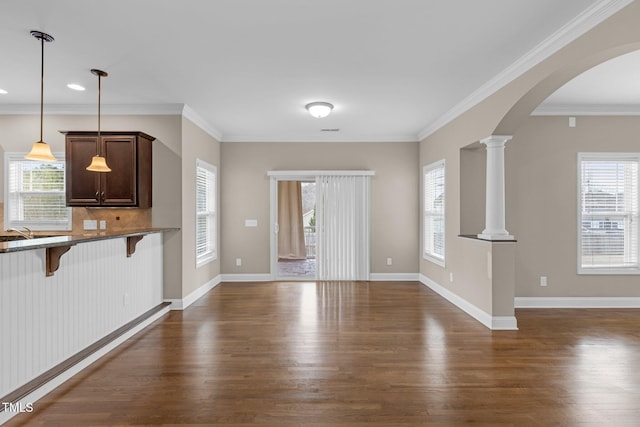 unfurnished living room with dark wood-style floors, baseboards, arched walkways, and ornate columns