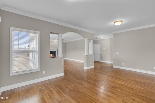 unfurnished living room with arched walkways, decorative columns, a glass covered fireplace, wood finished floors, and baseboards