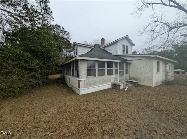 rear view of property featuring a yard, a chimney, and a sunroom