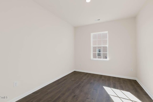 spare room featuring dark wood-style flooring, visible vents, and baseboards