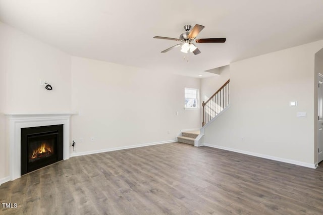 unfurnished living room featuring a warm lit fireplace, wood finished floors, baseboards, and stairs