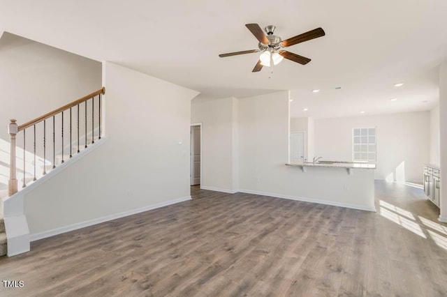 unfurnished living room with stairs, wood finished floors, and baseboards