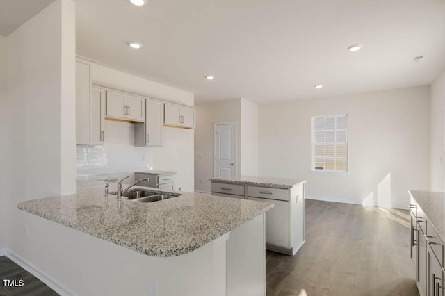 kitchen with dark wood-type flooring, a sink, light stone counters, and a center island