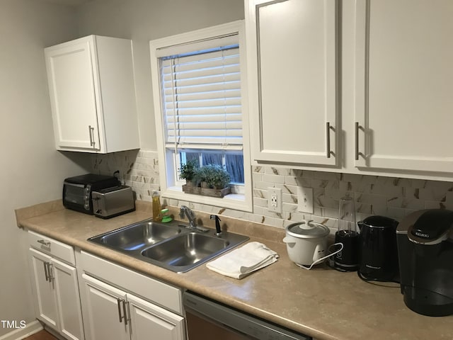 kitchen featuring white cabinets, dishwasher, backsplash, and a sink