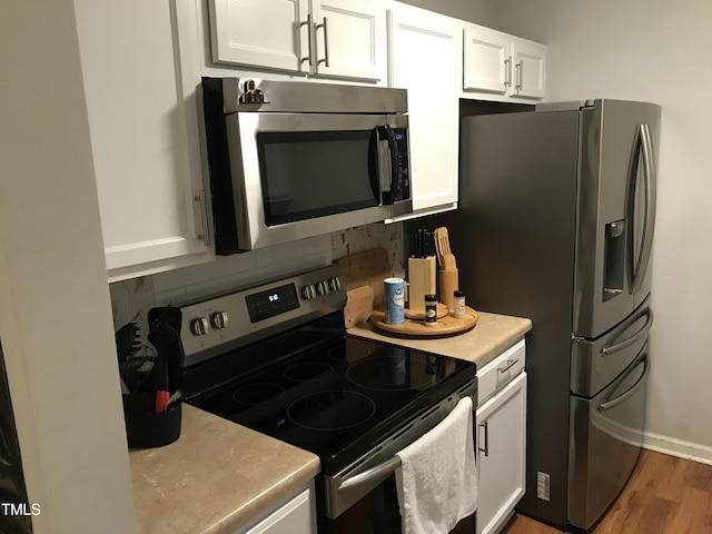 kitchen with stainless steel appliances, light countertops, backsplash, white cabinetry, and wood finished floors