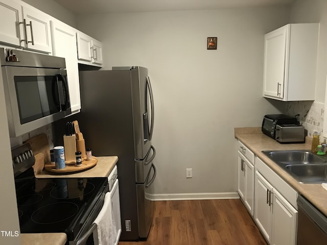 kitchen featuring stainless steel appliances, a sink, white cabinetry, tasteful backsplash, and dark wood finished floors