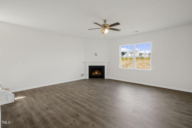 unfurnished living room with a warm lit fireplace, a ceiling fan, baseboards, and dark wood-style flooring