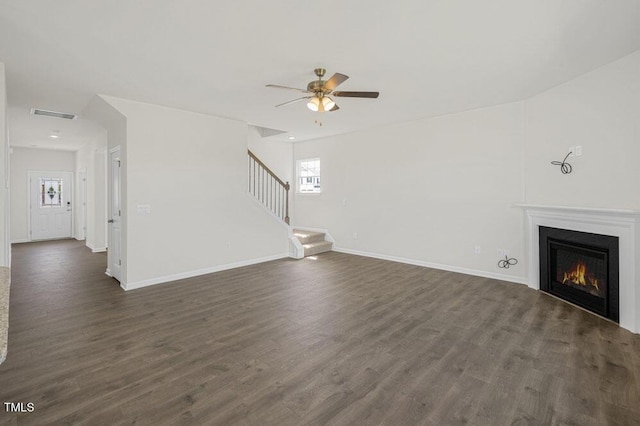 unfurnished living room featuring dark wood-style flooring, visible vents, stairway, a glass covered fireplace, and baseboards