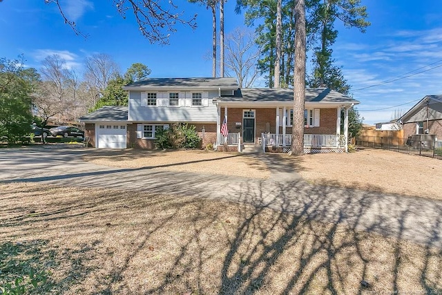 split level home with driveway, an attached garage, fence, a porch, and brick siding