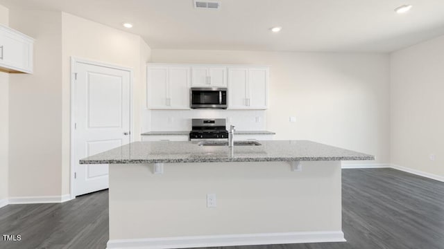 kitchen with appliances with stainless steel finishes, white cabinetry, a sink, and light stone countertops